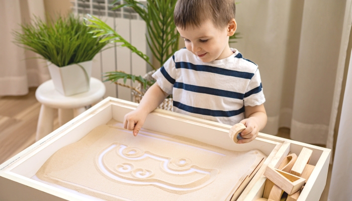 Closeup male kid hands drawing by fingers funny car character on sand wooden table therapy.