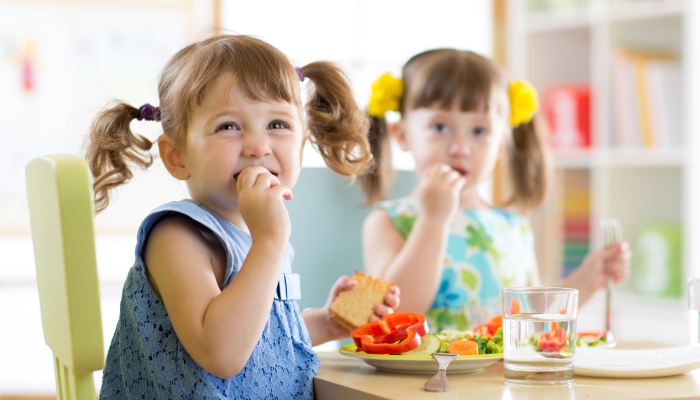 Cute little children eating food at daycare centre.