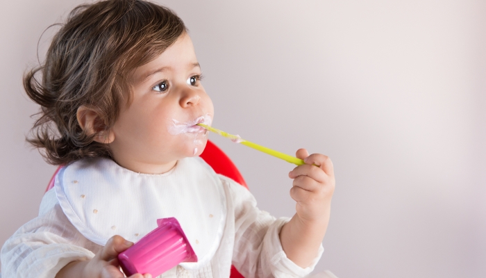 Cute toddler eating yogurt while looking at.