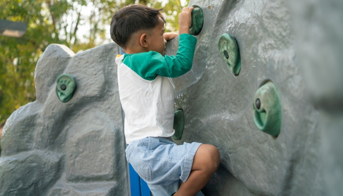 Happy asian boy climbing in outdoor playground public park outdoor activity.