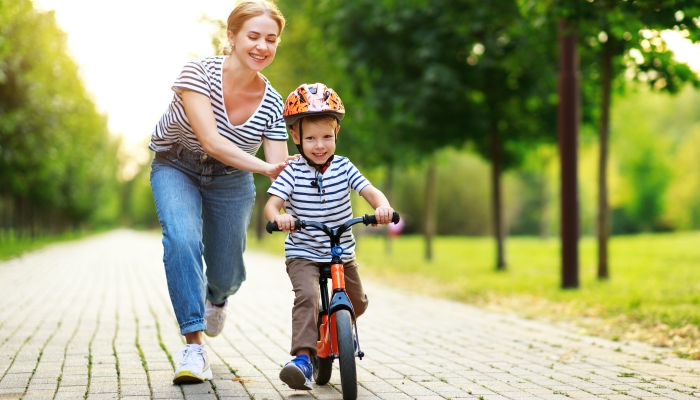 Happy family mother teaches child son to ride a bike in the Park in nature.