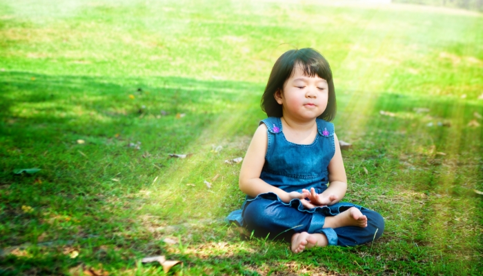 Little asian girl practicing mindfulness meditation outdoor in a park.