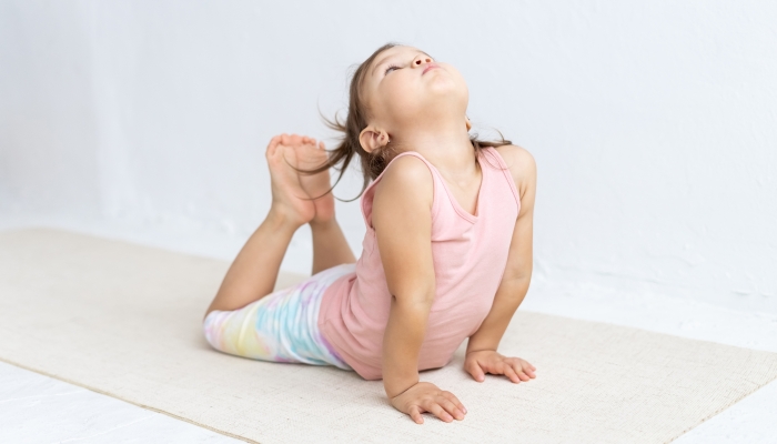 Little mixed race girl practices yoga on floor.