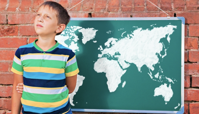 Meditative boy near chalkboard with drawing Earth map in the improvised outdoor class.