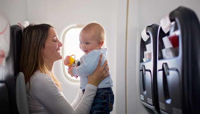 Mom playing and breastfeeding her toddler boy on board of aircraft, going on holiday.