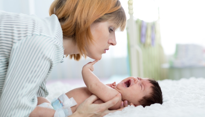 Mother comforts her crying newborn baby at home.