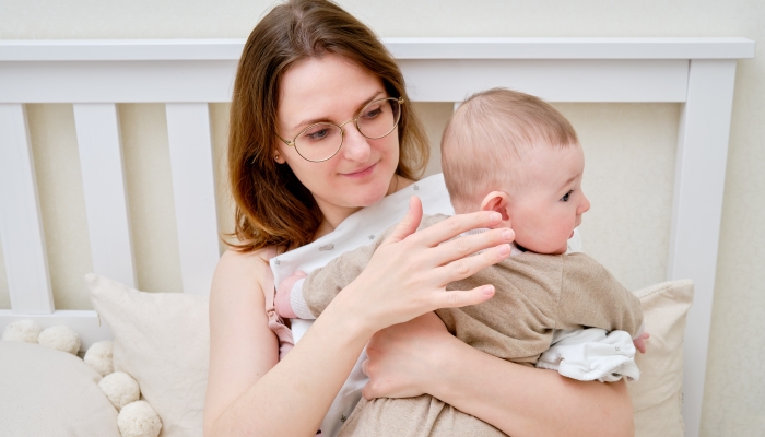 Mother woman holds an infant baby to regurgitate excess air after breastfeeding.