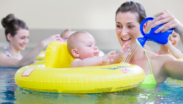 Mums and their children having fun together playing with toys at baby swimming lesson.