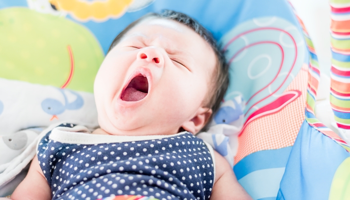 Portrait of a little adorable infant baby girl yawning before sleep on the bed indoors.