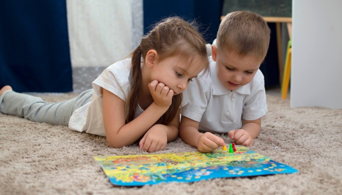 Portrait of two children lying on the floor and playing the board game walker in the nursery.