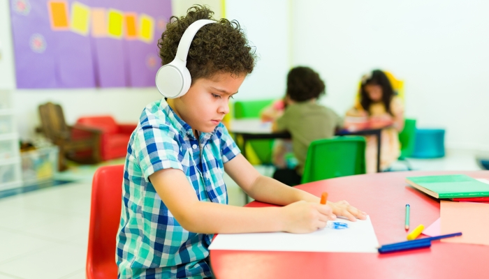 Preschool student boy with autism wearing headphones.