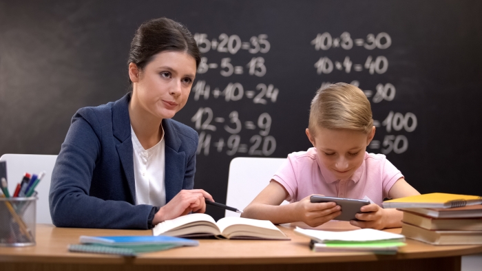 Strict teacher waiting naughty boy finishing playing on smartphone to teach him.