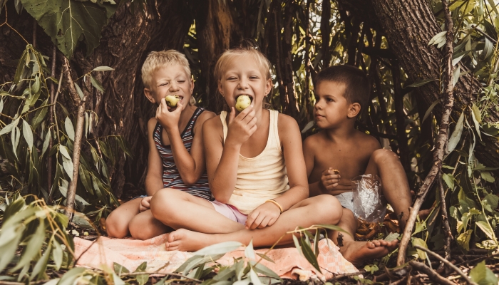 Three children play in a hut which they themselves have built from leaves and twigs.