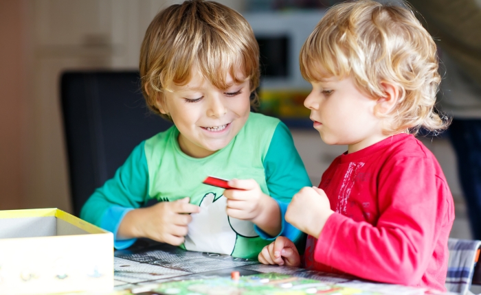 Two little blond kid boys playing together board game at home.