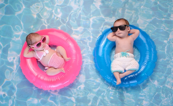 Two month old twin baby sister and brother sleeping on tiny, inflatable, pink and blue swim rings.