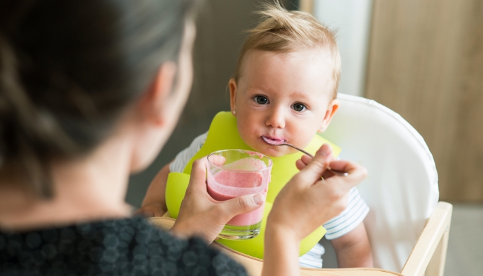 Unrecognizable mother feeding her baby daughter with yogurt.