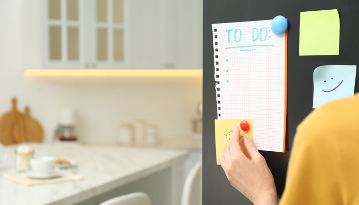 Woman putting blank to do list on refrigerator door in kitchen, closeup.