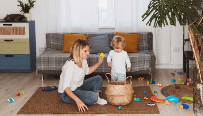 Housewife puts toys in the basket with her little son at home.