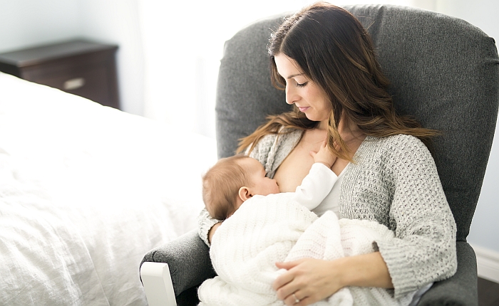 A young mother holding her baby child sitting on a chair.