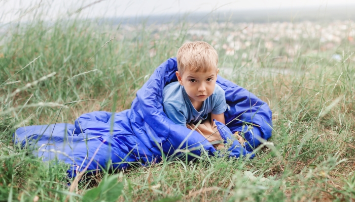 Cute boy having rest and dreaming alone in sleeping bag.