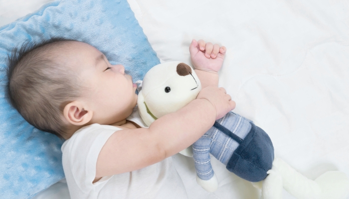 Cute newborn sleeps with a toy teddy bear on comfortable bed.