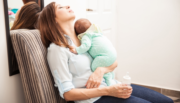 Portrait of an exhausted mother taking a nap while holding her newborn baby at home.