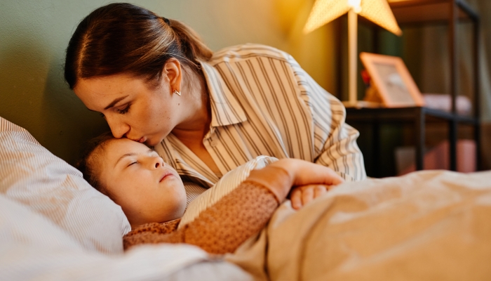 Portrait of caring mother kissing child with down syndrome at bedtime.