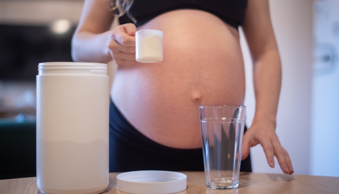 Pregnant woman holding a scoop with whey.