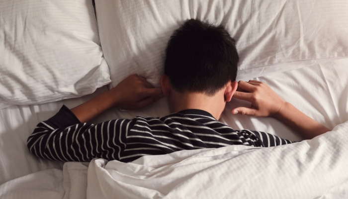 Preteen tween boy covering ears with his fingers in bed.