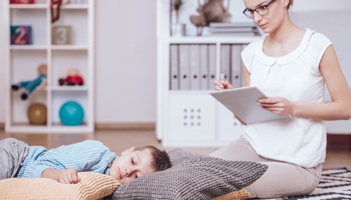 Psychotherapist observing behaviors of a boy with Asperger syndrome sleeping on pillows.