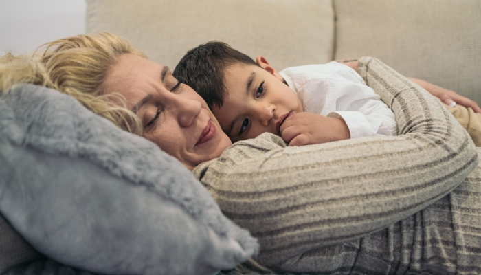 Woman lying and sleeping on the couch with her autistic young son.