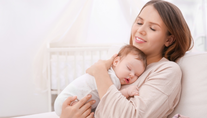 Young mother holding sleeping baby at home.