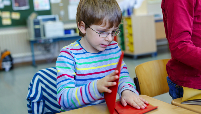 A boy with glasses folding a large paper for origami.