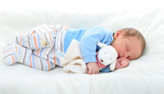 Cute baby with toy sleeping on white blanket.