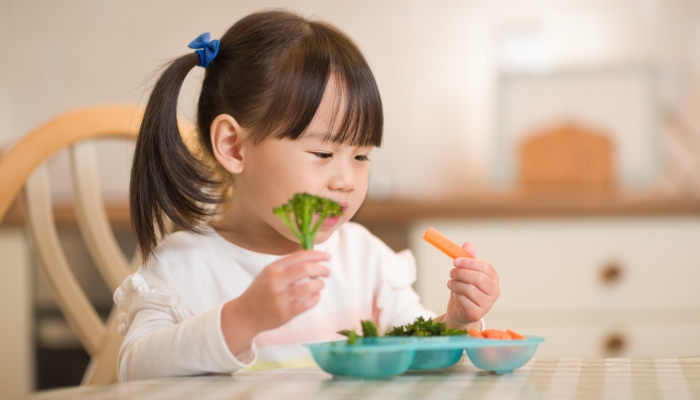 young girl eating fresh green vegetables against real kitchen background.