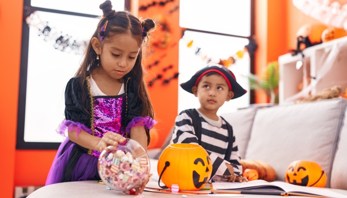 Adorable boy and girl having halloween party holding candies at home.