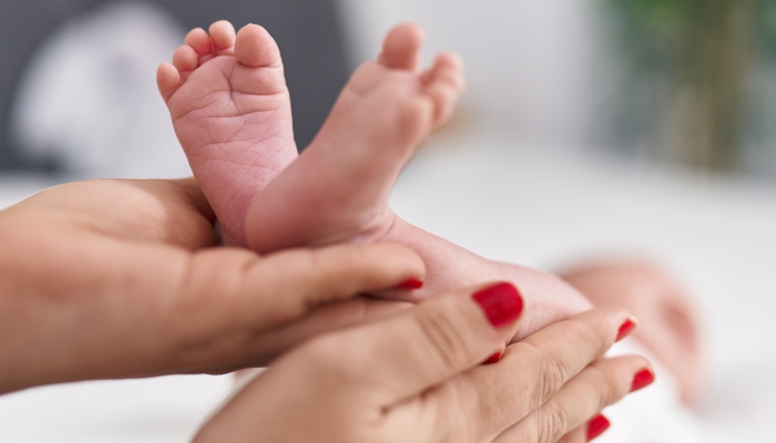 Adorable caucasian baby lying on bed having legs massage at bedroom.