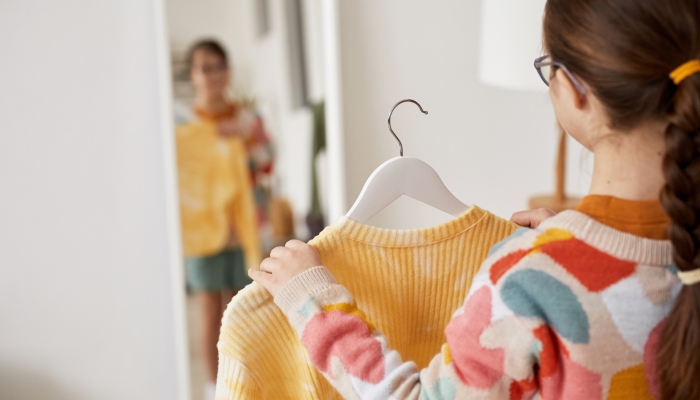 Back view at teenage girl choosing clothes and looking at mirror at home.