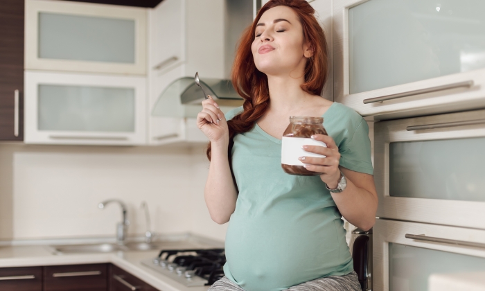 Beautiful pregnant woman enjoying eating chocolate paste.