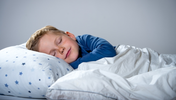 Child boy sleep in bed on pillow with blue stars and white blanket.