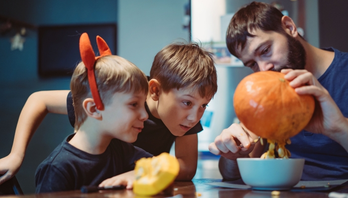 Children with father carving a traditional Jack lantern from pumpkin.