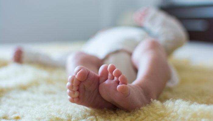 Close-up of unrecognizable cute baby shaking feet while lying in bed.
