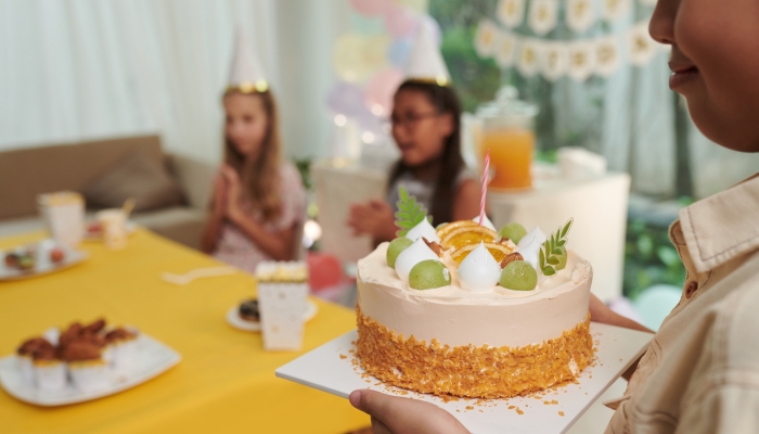 Smiling birthday boy bringing cake with candle to table.