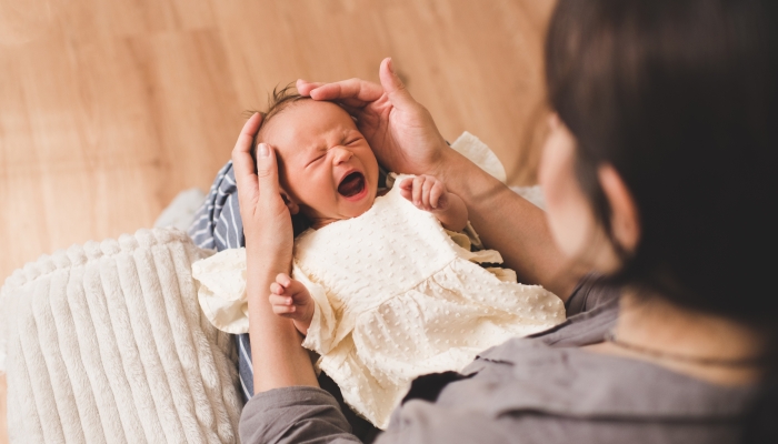 Crying baby girl wake up on mother hands in room.