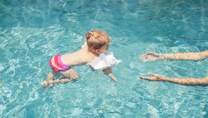 Cute little baby swimming to father in a pool,.