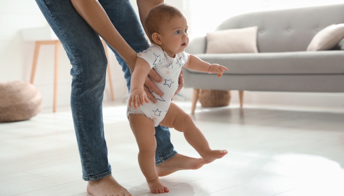 Father supporting his baby daughter while she learning to walk at home.