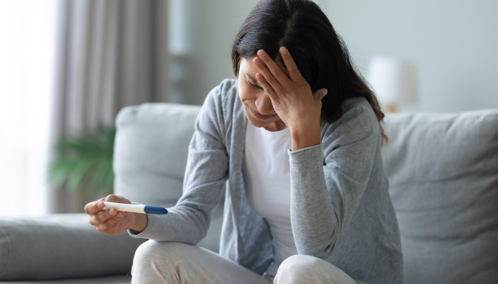 Frustrated unhappy mixed race woman sitting in living room, holding quick plastic test.