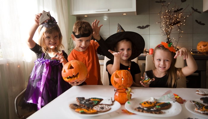 Group of children in masquerade costumes paint gingerbread for the halloween holiday at home in the kitchen.