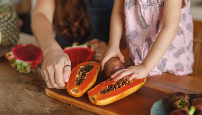 Hands of little girl and her mother touch papaya tropical fruit.