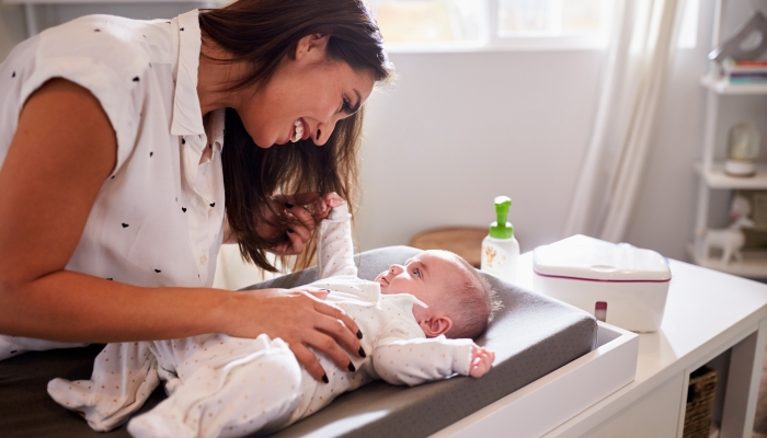 Happy mother changing the diaper of her baby at home on a changing table.